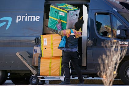 Una persona que entrega mercancía de Amazon Prime acomoda paquetes al hacer una parada en un edificio de apartamentos, el martes 28 de noviembre de 2023, en Denver. (AP Foto/David Zalubowski)