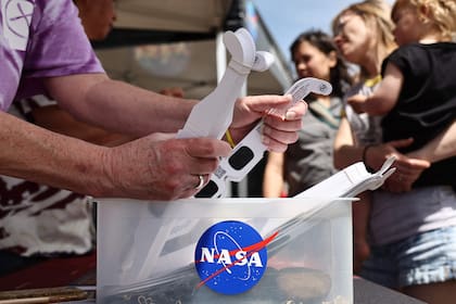 Una persona recoge anteojos gratuitos para eclipses solares, proporcionados por la NASA en un stand de información de la NASA durante la celebración en la ciudad del eclipse solar del 8 de abril el 7 de abril de 2024 en Russellville, Arkansas