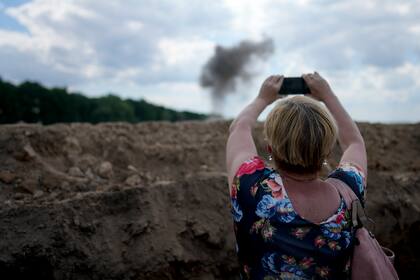 Una reportera toma una foto del humo que deja tras de sí la explosión de una mina terrestre por parte de un equipo de expertos ucranianos que trabajan en la limpieza de un campo próximo a la capital, Kiev, el 9 de junio de 2022. (AP Foto/Natacha Pisarenko)