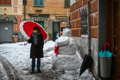 Una residente con barbijo junto a un muñeco de nieve en una calle del pueblo de Sassello, Liguria, luego de una nevada nocturna el 2 de diciembre de 2020