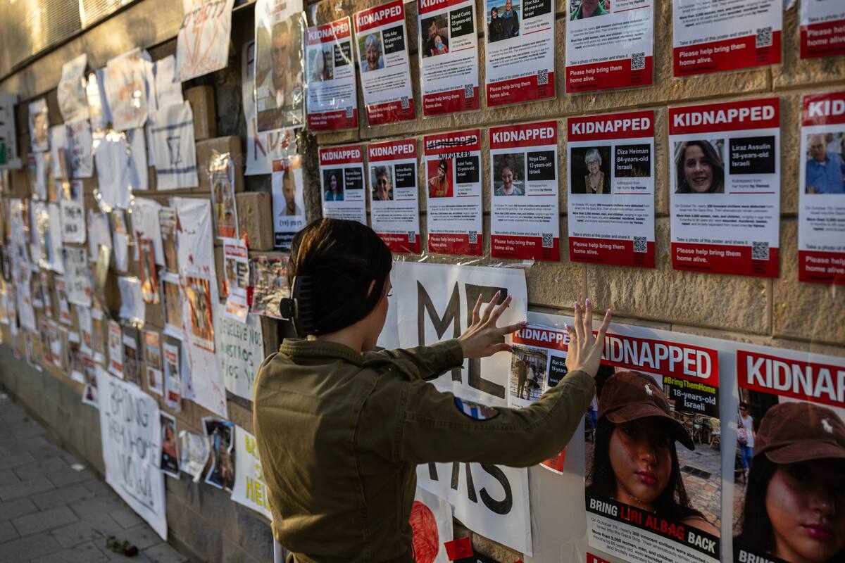Una soldado israelí pega una foto de su amigo Ron Sherman, quien se cree que fue secuestrado por Hamas, en una pared cerca del Ministerio de Defensa en Tel Aviv, Israel. (Tamir Kalifa/The New York Times)