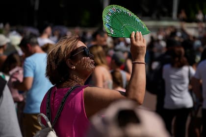 Una turista usa un abanico para protegerse la cara del sol mientras espera ver la ceremonia del cambio de guardia en las afueras del Palacio de Buckingham, durante la ola de calor