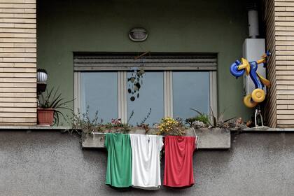 Una ventana con tres remeras que representan la bandera italiana, en Roma