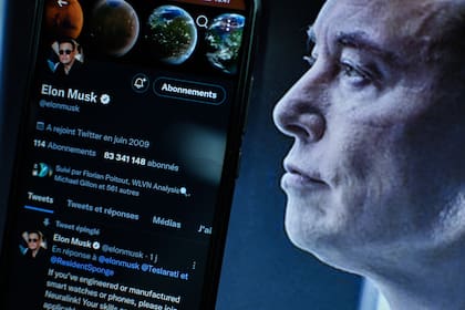 Una vista del logotipo de la empresa estadounidense de redes sociales Twitter en la pantalla de un smartphone junto a un retrato del empresario Elon Musk