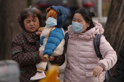 Unas mujeres llevan a un niño pequeño por una calle en Pekín