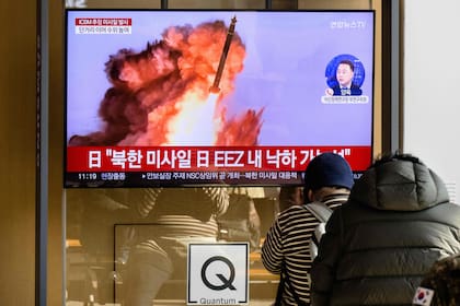 Unas personas se sientan cerca de un televisor que muestra un noticiero con imágenes de archivo de una prueba de misiles de Corea del Norte, en una estación de tren en Seúl el 18 de noviembre de 2022.