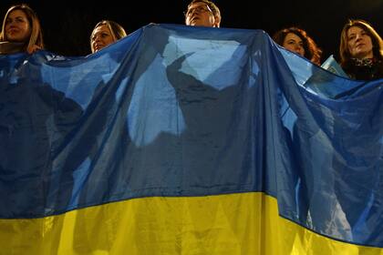 Unas personas sostienen una enorme bandera ucraniana durante un evento en Kramatorsk, Ucrania, el miércoles 23 de febrero de 2022. (AP Foto/Andriy Andriyenko)
