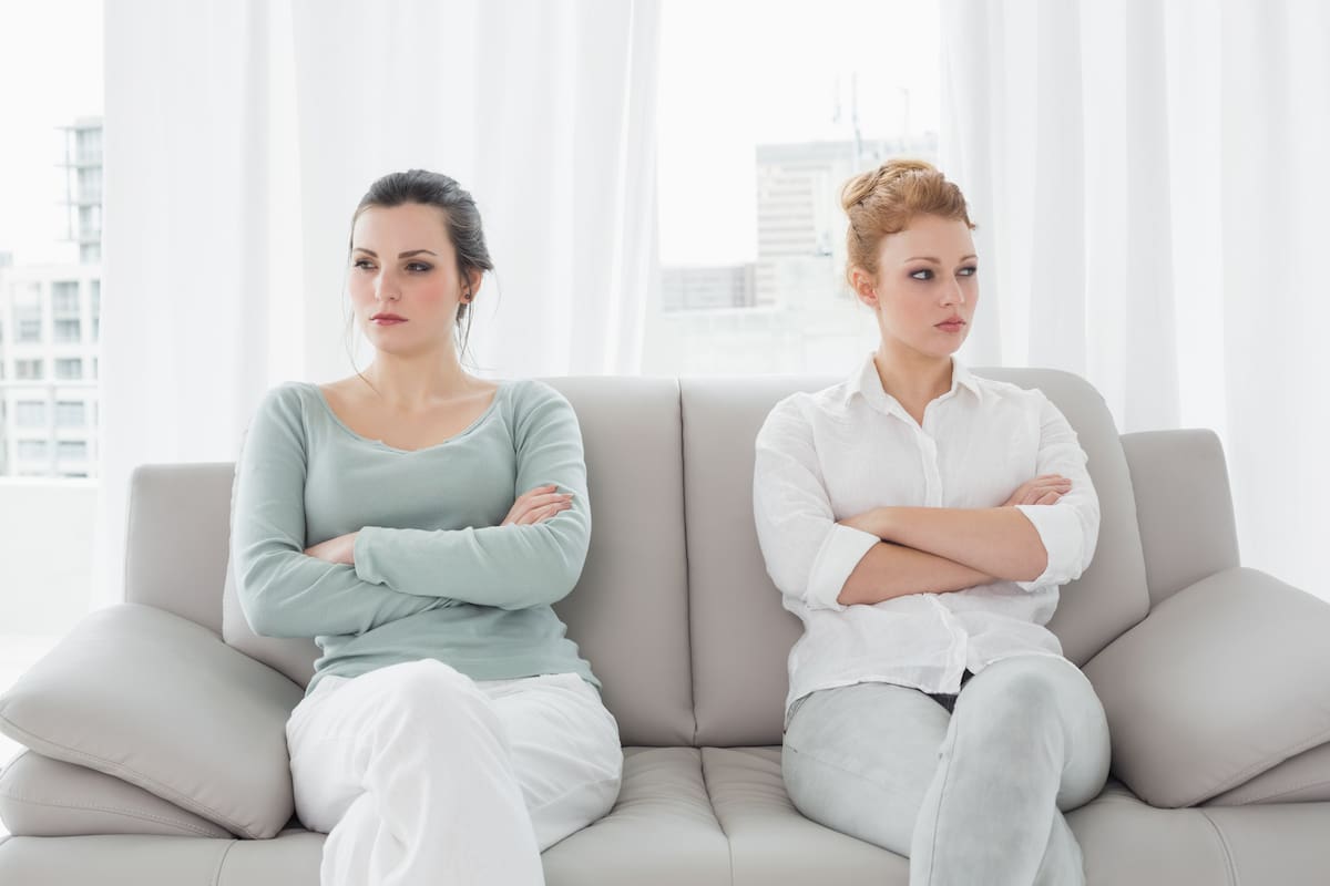 Unhappy young female friends not talking after argument at home on the couch