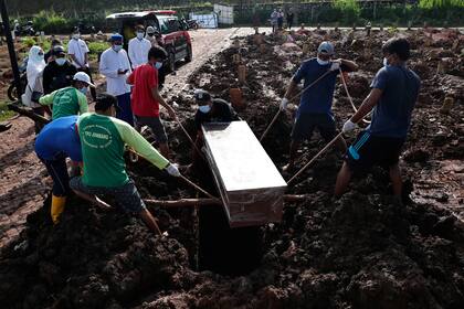 Unos trabajadores bajan un ataúd durante la inhumación de una víctima fatal de Covid-19, en una zona especial para esos cadáveres en el cementerio público de Jombang, el lunes 21 de junio de 2021 en Tangerang, en las afueras de Yakarta, Indonesia