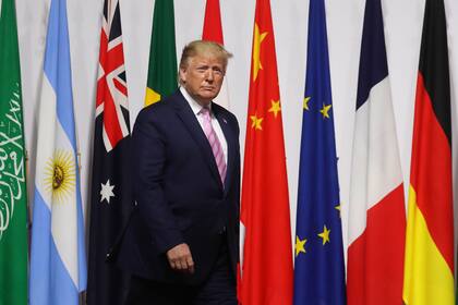 US President Donald Trump walks past G20 member flags as he is welcomed by Japanese Prime Minister Shinzo Abe prior to the family photo at the G20 Osaka Summit in Osaka on June 28, 2019. (Photo by Ludovic MARIN / POOL / AFP)