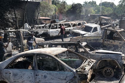 Varias personas buscan piezas rescatables de coches quemados en un taller mecánico incendiado durante la violencia desatada por pandillas armadas en Puerto Príncipe, Haití, el lunes 25 de marzo de 2024. (AP Foto/Odelyn Joseph)