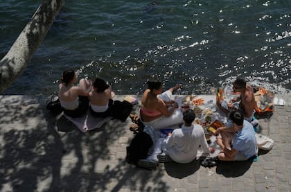 Varias personas disfrutan de un picnic a orillas del río Sena durante un día soleado, el lunes 25 de mayo de 2026, en París