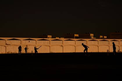 Varias personas juegan al críquet en las calles de Doha, Qatar, el 25 de noviembre de 2022. Los trabajadores que construyeron los estadios del Mundial, las carreteras y las estaciones de metro de Qatar llenaban solares vacíos al despuntar el alba el viernes para jugar al deporte que les toca más de lleno el corazón: críquet. (AP Foto/Abbie Parr)