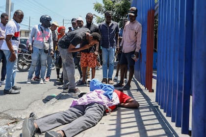 Varias personas observan el cuerpo de un hombre tendido en la calle del barrio de Delmas 30 en Puerto Príncipe, Haití, el lunes 1 de abril de 2024