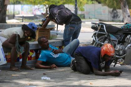 Varias personas se refugian de los disparos durante choques entre la policía y bandas armadas en las inmediaciones del Palacio Nacional, en Puerto Príncipe, Haití, el 8 de abril de 2024. (AP Foto/Odelyn Joseph)