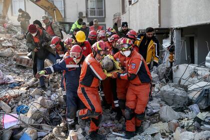 Varias personas sentadas el lunes 13 de febrero de 2023 junto a una vivienda destrozada mientras esperan que los cuerpos de sus amigos y familiares sean sacados de los escombros luego de un sismo en Antioquía, Turquía. (AP Foto/Bernat Armangue)