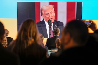 Varias personas siguen la toma de posesión de Donald Trump en pantallas en la casa de Ucrania, en el Foro Económico Mundial, en Davos, Suiza, el 20 de enero de 2025. (AP Foto/Markus Schreiber)