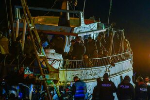 Varios policías, abajo, aguardan frente a un barco pesquero con unos 500 migrantes la madrugada del sábado 11 de marzo de 2023 en el puerto de Crotone, en el sur de Italia.