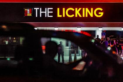 Varios transeúntes observan cómo los policías de Miami Gardens trabajan en los alrededores del restaurante The Licking después de que, según versiones, varias personas resultaran heridas a disparos la noche del jueves 5 de enero de 2023 en Miami Gardens, Florida. (Al Díaz/Miami Herald vía AP)