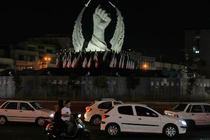 Varios vehículos pasan ante un monumento que muestra el puño cerrado del fallecido líder supremo iraní Alí Khamenei