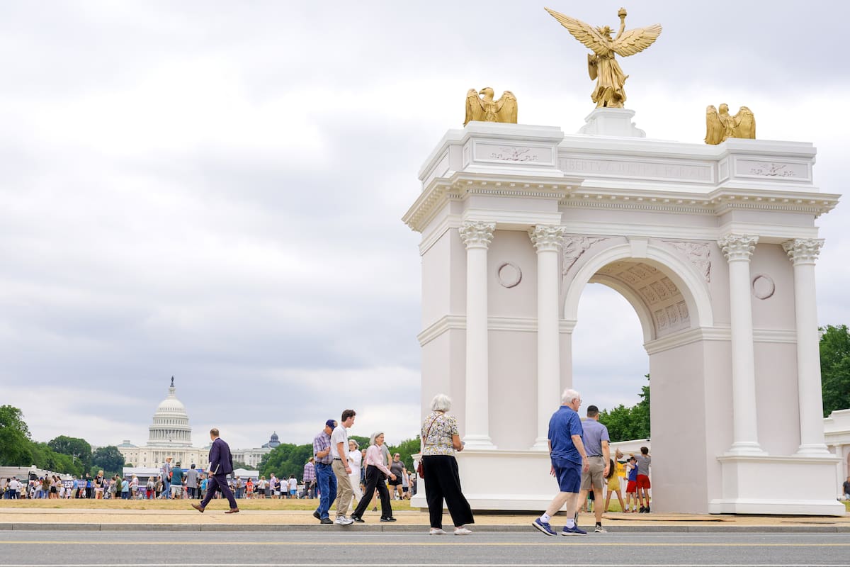 Varios visitantes recorren la Gran Feria Estatal de Estados Unidos con un modelo del arco del triunfo y el Capitolio estadounidense en el fondo, el miércoles 8 de julio de 2026, en Washington