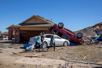 Vecinos pasan ante una casa dañada por el tiempo en Wheatland Drive y Conway Drive el lunes 27 de febrero de 2023 en Norman, Oklahoma, tras una serie de tormentas y tornados en Oklahoma durante la noche. (AP Foto/Alonzo Adams)