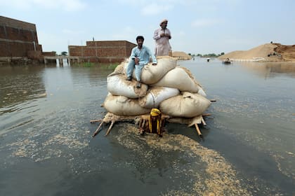Víctimas de inundaciones provocadas por las lluvias monzónicas usan una balsa improvisada con el fin de transportar paja para el ganado, el 5 de septiembre de 2022, en Jaffarabad, un distrito de la provincia de Baluchistán, en el suroeste de Pakistán. (AP Foto/Fareed Khan)