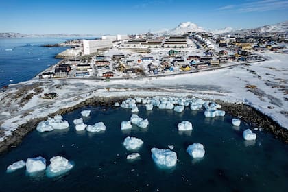 Vista aérea tomada el 11 de marzo de 2025, muestra icebergs flotando en aguas iluminadas por el sol, con edificios al fondo frente a Nuuk, Groenlandia