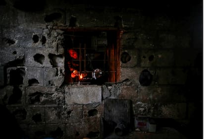 Una mujer se ve a travez de la venta de su cocina mientras prepara la comida a la luz de las velas en Beit Lahiya, al norte de la Franja de Gaza