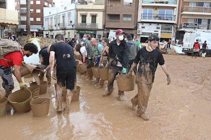 Voluntarios cargan cubetas con lodo tras las inundaciones en Paiporta, cerca de Valencia, España, el 3 de noviembre de 2024. (AP Foto/Hugo Torres)
