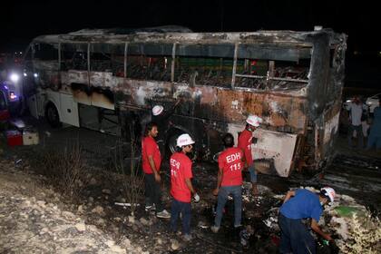 Voluntarios reunidos en torno a un autobús quemado en una autopista en Nooriabad, Pakistán, el jueves 13 de octubre de 2022. (AP Foto/Pervez Masih)