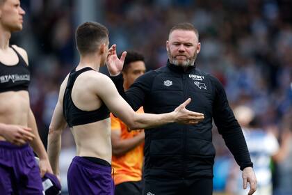 Wayne Rooney (con barba) saluda a sus jugadores tras la derrota 1-0 ante Queens Park Rangers, que condenó al Derby County al descenso a la tercera división del fútbol inglés el 18 de abril del 2022 en Londres. Rooney dirige al Derby desde noviembre del 2020. (Steven Paston/PA vía AP)