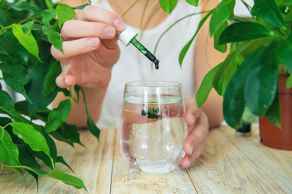 Woman dripping chlorophyll supplement into a glass of water. Selective focus. Drink.
