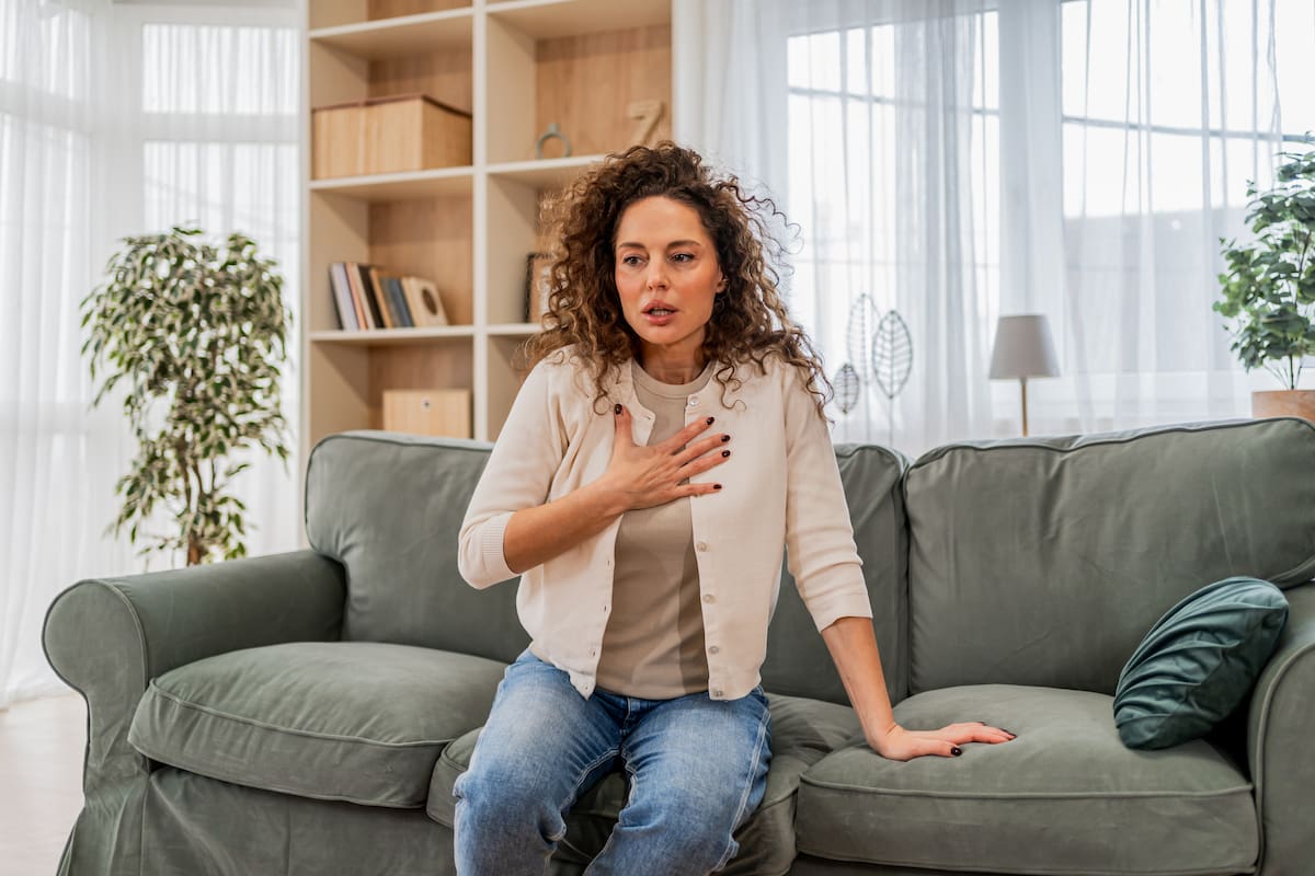 Woman experiencing severe chest pain and difficulty breathing while sitting on a couch in her living room