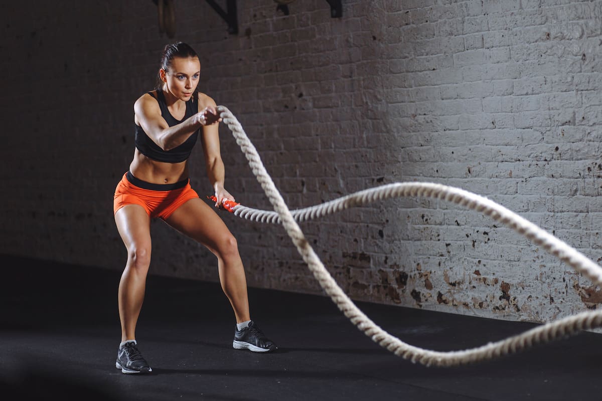 Woman training with battle rope in cross fit gym