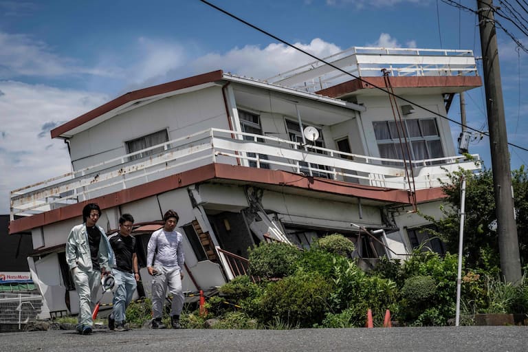 Workers walk past a damaged house and partially collapsed in Yatsushiro, Kumamoto prefecture on July 29, 2026, after an earthquake struck southwestern Japan the previous day. (Photo by Yuichi YAMAZAKI / AFP)