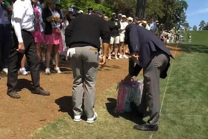 Xander Schauffele y el árbitro buscan la pelota dentro de la bolsa de la espectadora; una situación inusual en plena vuelta del Masters