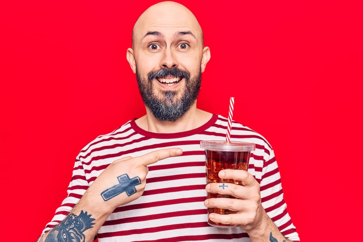 Young handsome man drinking glass of cola beverage smiling happy pointing with hand and finger