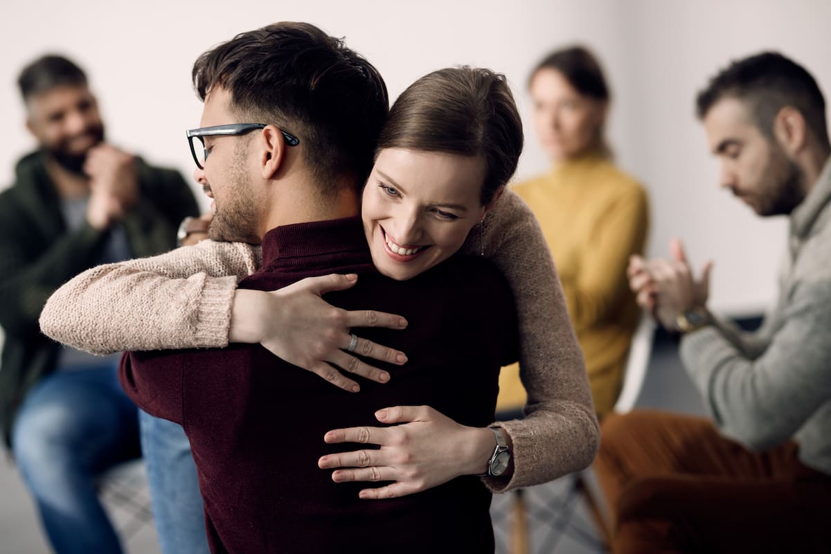 Young happy couple embracing while taking a part in group therapy at community center.
