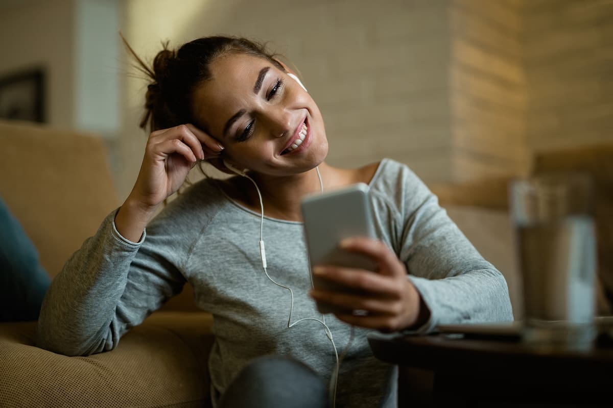 Young happy woman enjoying in the evening while using smart phone in the living room.
