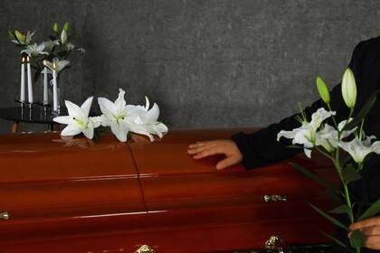Young man with white lilies near casket in funeral home, closeup