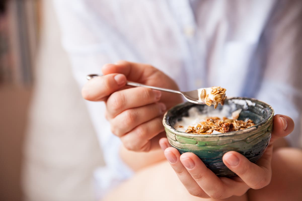 Young woman with muesli bowl. Girl eating breakfast cereals with nuts, pumpkin seeds, oats and yogurt in bowl. Girl holding homemade granola. Healthy snack or breakfast in the morning..