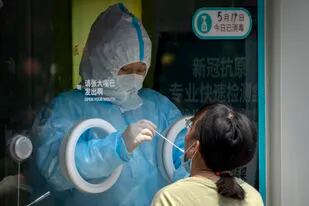 Un trabajador sanitario, vestido con un traje de protección, toma una muestra para realizar una prueba de detección del coronavirus, en Beijing, el 19 de mayo de 2022. (AP Foto/Mark Schiefelbein)
